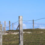Barrière en bois et fil de fer sur une dune. Ciel bleu.